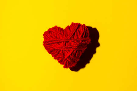 red knitted heart for Valentine's day on a yellow background, isolate .close upの写真素材
