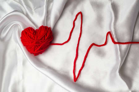 white silk fabric with bends and a red knitted heart with a pulse line for Valentine's Day, copy space. top viewの写真素材