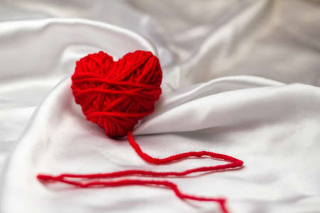 white silk fabric with bends and a red knitted heart with a pulse line for Valentine's Day, copy space. bot viewの写真素材