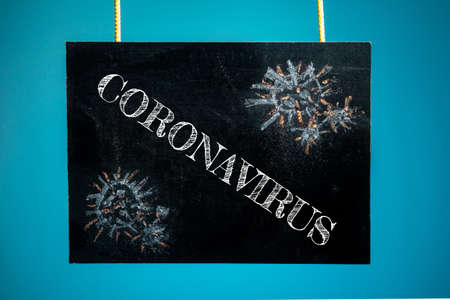 A chalk board is hung with the inscription "coronavirus" and a pattern of virus cells on a blue background. copy spaceの写真素材