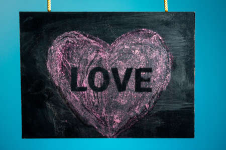 Chalk board is hanging with the inscription "love" and a pattern of a pink heart on a blue background. copy spaceの写真素材