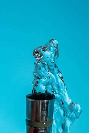 Metal tap from which water pours to the top on a blue background copy space close upの写真素材