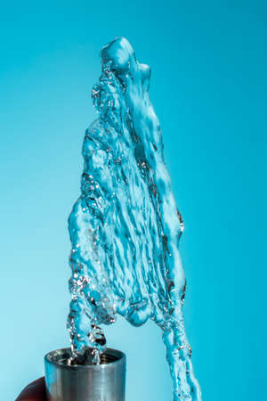 Metal tap from which water pours to the top on a blue background copy space close up