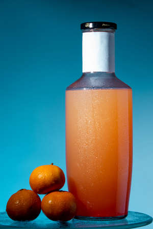 bottle with juice and tangerines on glass with drops of mocap on a blue background, close up, copy...