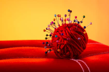 a red skein of thread stuck a lot of needles on red leather on an orange background. close up copy spaceの写真素材