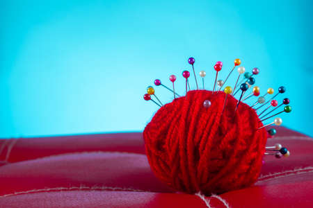 a red skein of thread stuck a lot of needles on red leather on a blue background. close up copy spaceの写真素材