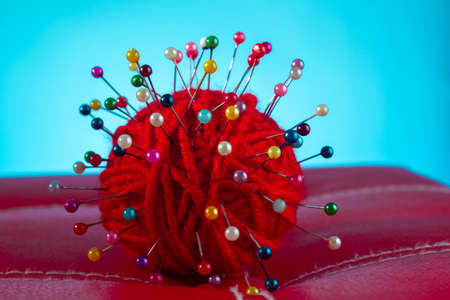 a red skein of thread stuck a lot of needles on red leather on a blue background. close up copy...