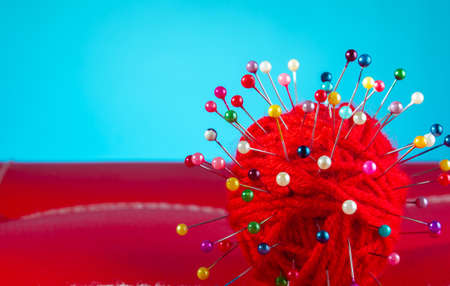a red skein of thread stuck a lot of needles on red leather on a blue background. close up copy spaceの写真素材
