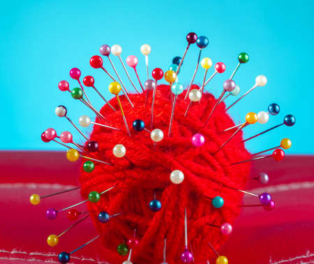 a red skein of thread stuck a lot of needles on red leather on a blue background. close up copy spaceの写真素材