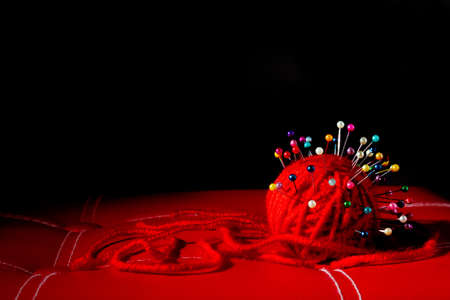 a red skein of thread stuck many needles into red leather on a black background. close copy spaceの写真素材