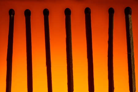 silhouette of seven matches with a red head in a row on a Lush Lava background. close up copy space