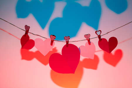 Paper hearts of red clothespins with a heart on a rope with a shadow. Valentine's Day love. blue-pink background. copy spaceの写真素材
