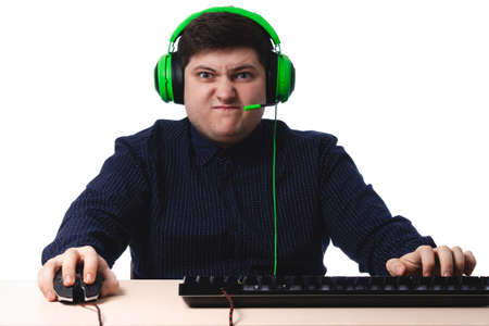 A young guy in a dark blue shirt green headphones gamer angry on a white background. isolate. copy...
