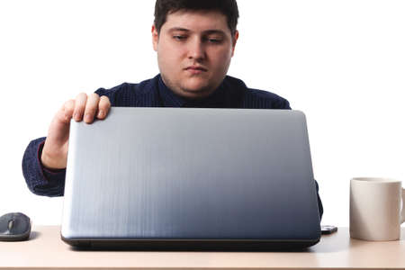 A young guy in a dark blue shirt opens a laptop next to an office, business cup of coffee on a white background. isolate. copy spaceの写真素材