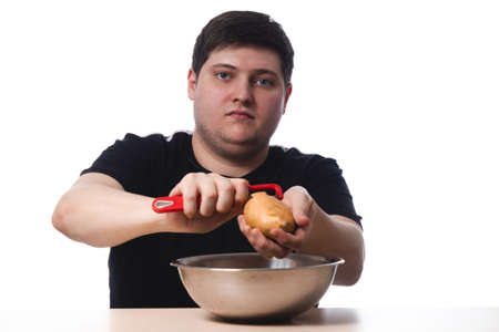 A young guy in a black T-shirt peels potatoes. on white background. isolate. copy spaceの写真素材