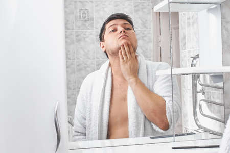 a man in a white bathrobe looks in the mirror in the bathroom.の写真素材