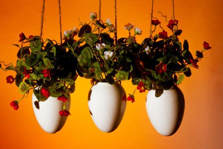 three hanging pots with artificial flowers decorative element of the house on an orange background copy spaceの写真素材