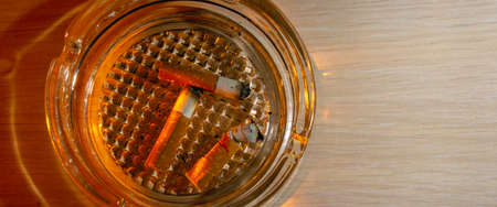 Glass ashtray with three cigarette butts on wood background copy spaceの写真素材