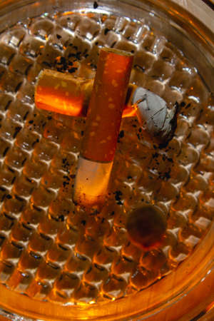 Glass ashtray with three cigarette butts on wood background copy space close upの写真素材