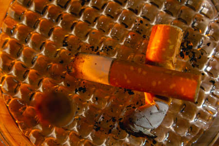 Glass ashtray with three cigarette butts on wood background copy space close upの写真素材