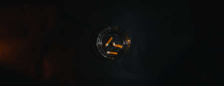 Glass ashtray with three cigarette butts with orange modeling light on a black background copy spaceの写真素材