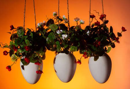 three hanging pots with artificial flowers decorative element of the house on an orange background copy spaceの写真素材