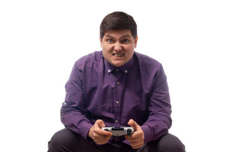 A fat man in a purple shirt is playing on a gamepad, is tense, angry, on a white background. isolate. copy spaceの写真素材