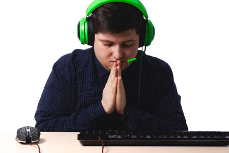 A young guy in a dark blue shirt green headphones gamer prays on a white background. isolate. copy spaceの写真素材