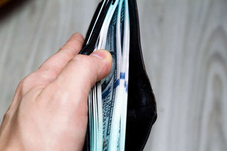 a bundle of hundred-dollar banknote in a black leather wallet in his hand. view from the side. close upの写真素材