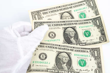 a hand in a white glove holds three one-dollar bills on a white background.の写真素材