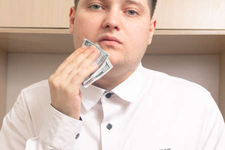 Caucasian man wipes his mouth hundred dollar bills in a white shirt in the officeの写真素材