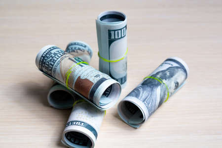 one hundred dollar bills knitted by elastic in rolls on a light wooden table. side view. to closeの写真素材