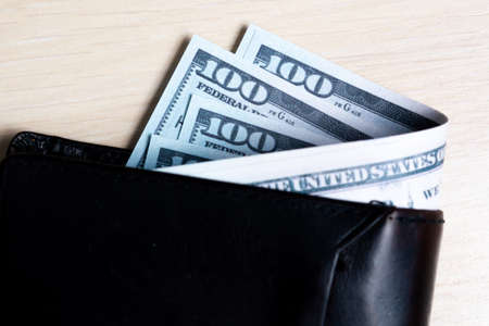 bundle of dollar bill in black leather wallet on a light wooden background. view from above. to closeの写真素材
