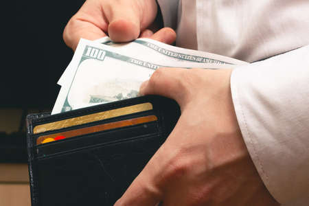 man pulls out of the wallet hundred dollar bills in a white shirt in the office
