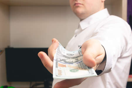 Caucasian man holds out to the camera a bundle of hundred-dollar bills in a white shirt in the officeの写真素材