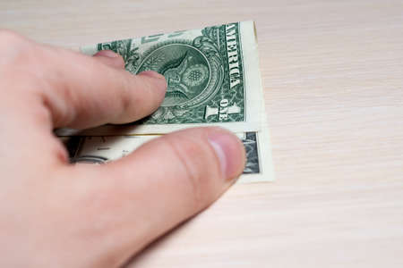 hand holds out a one-dollar bill on a light wooden table. side view. to close