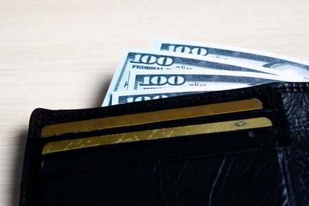 a bundle of hundred-dollar banknote in a black leather wallet on a light wooden. view from the side....