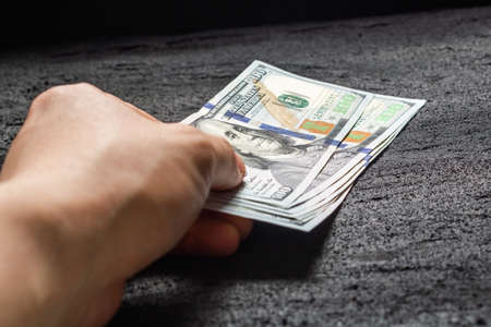 hand lays a pack of hundred-dollar bills on black concrete dark background .copy space