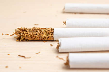 five cigarettes and one got out on half tobacco on a light wooden