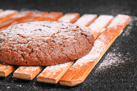 chocolate oatmeal cookies sprinkled with powdered sugar lies on a bamboo plate on black concreteの写真素材