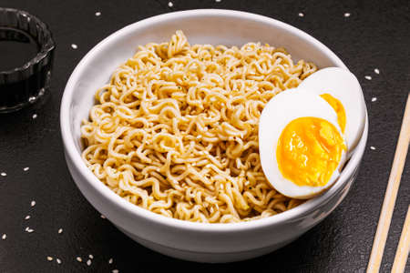 noodles in a plate with sesame seeds and soy sauce, bamboo sticks, boiled eggs on a black table close-up. side view .copy space.の写真素材