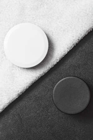 cosmetic black jar on a black table white cosmetic jar on a white towel .mocap, flat lay, top view, close up, copy space vertical orientationの写真素材