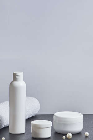 white cosmetic jars for the bath a long tube of pearl towel on a gray background. copy space. mockup. vertical orientationの写真素材