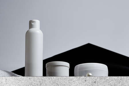 white cosmetic jars for a bathtub a long tube of towel is pearl on a marble plate on a gray background and a black triangle. copy space. mockup. bot viewの写真素材