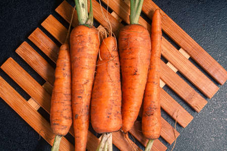 not washed in the ground a young orange carrot with sprouts on a bamboo leaf on a black table. copy...