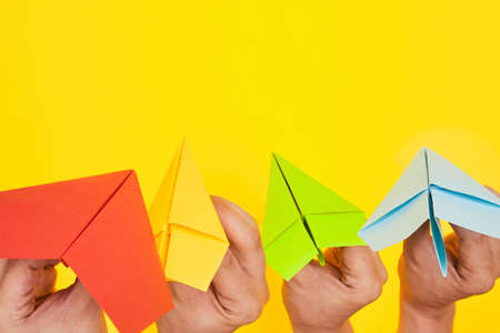 Hands throw paper planes multicolored on yellow background copy space one