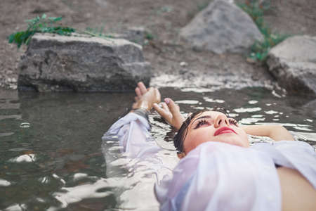 girl in the river on a stone in a white shirt, one