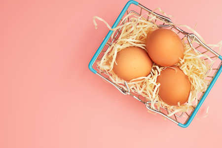 chicken eggs in a shopping cart on a pink pastel background, copy space, flatlayの写真素材