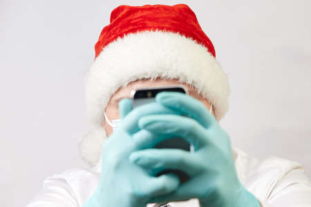 coronavirus concept, man in santa hat and medical mask with phone on white background