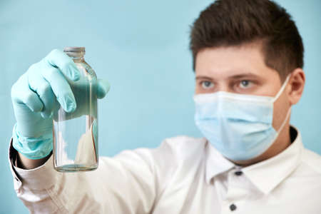coronavirus concept man in medical mask looks at bottle on blue background